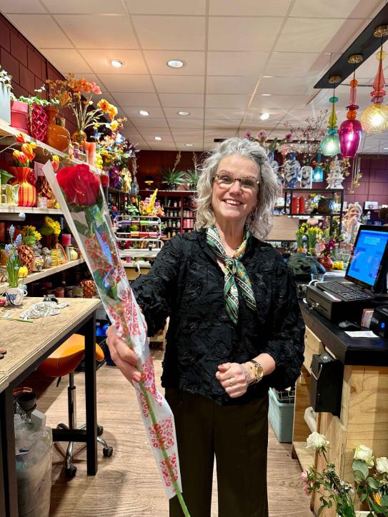 losse roos kopen als valentijnscadeau, Anja met glimlach en rode kunstroos in valentijnsdag papiertje