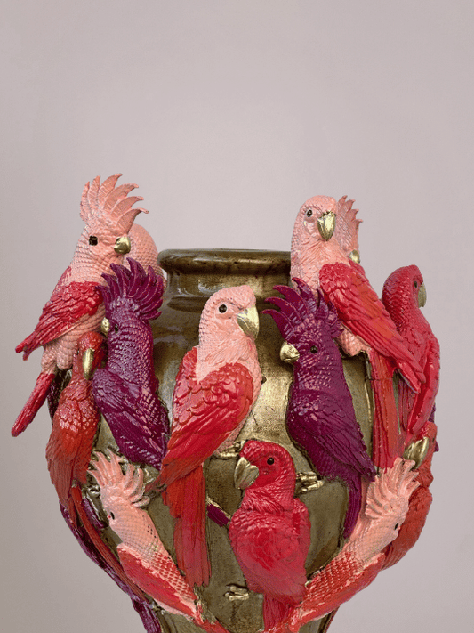 Close-up van kaketoevogel in rood en roze op gouden vaas, met 3D-effect en opvallende details.