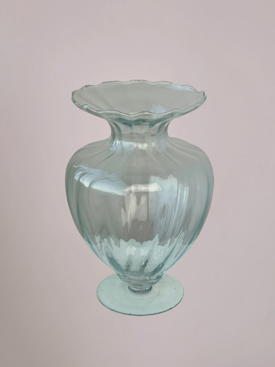 Doorzichtige vaas van boven met diepe ribbels, smalle bovenhals en ronde voet, met lichtroze achtergrond.