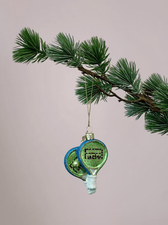Vondels kerstbal padelrakets in kerstboom, groen met blauwe rand en witte handvaten, origineel ornament met lichtroze achtergrond.