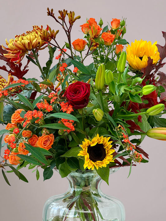 Close-up van herfstboeket rond in ronde vaas met zonnebloemen, rode rozen, trosrozen, kangaroepootjes en herfstchrysanten, perfect voor herfstdecoratie