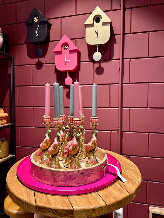 Gouden kandelaar met vogel gestyled op een houten dienblad, voor een donkerroze muur, gecombineerd met zachte woonaccessoires.