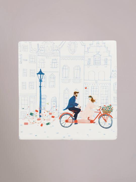 Tegel It’s Official! met een pasgetrouwd stel op een tandemfiets, confetti en een rood hartje erboven, symbool voor romantiek en feestelijkheid.