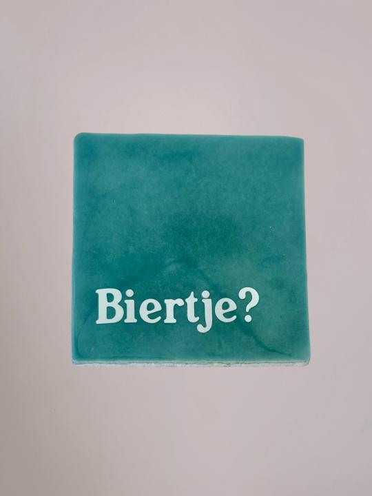 Blauw Yett Agenturen tegeltje van 10x10 cm met de tekst 'Biertje?' en een glanzende afwerking. Grappig cadeau voor bierliefhebbers.