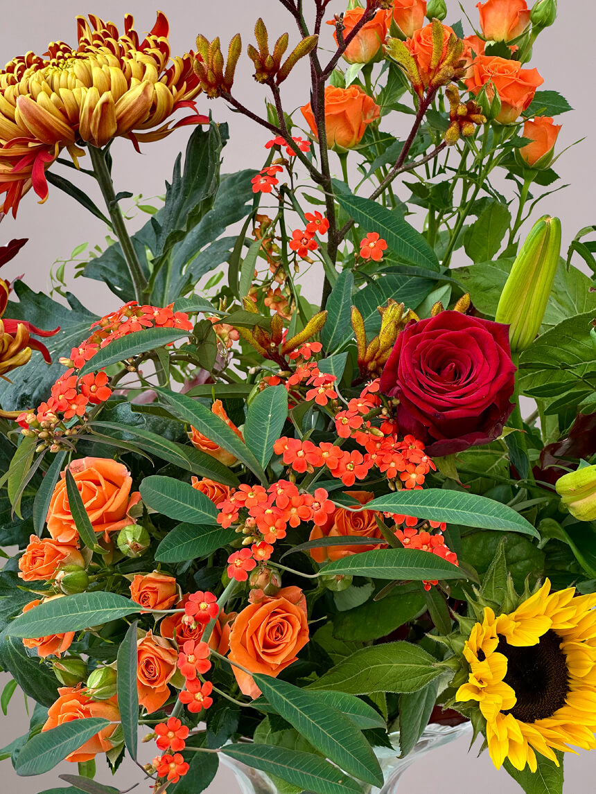 Detailfoto van herfstboeket rond met zonnebloem, rode roos, trosroos, kangaroepootje en herfstchrysant, seizoensbloemen in warme herfstkleuren
