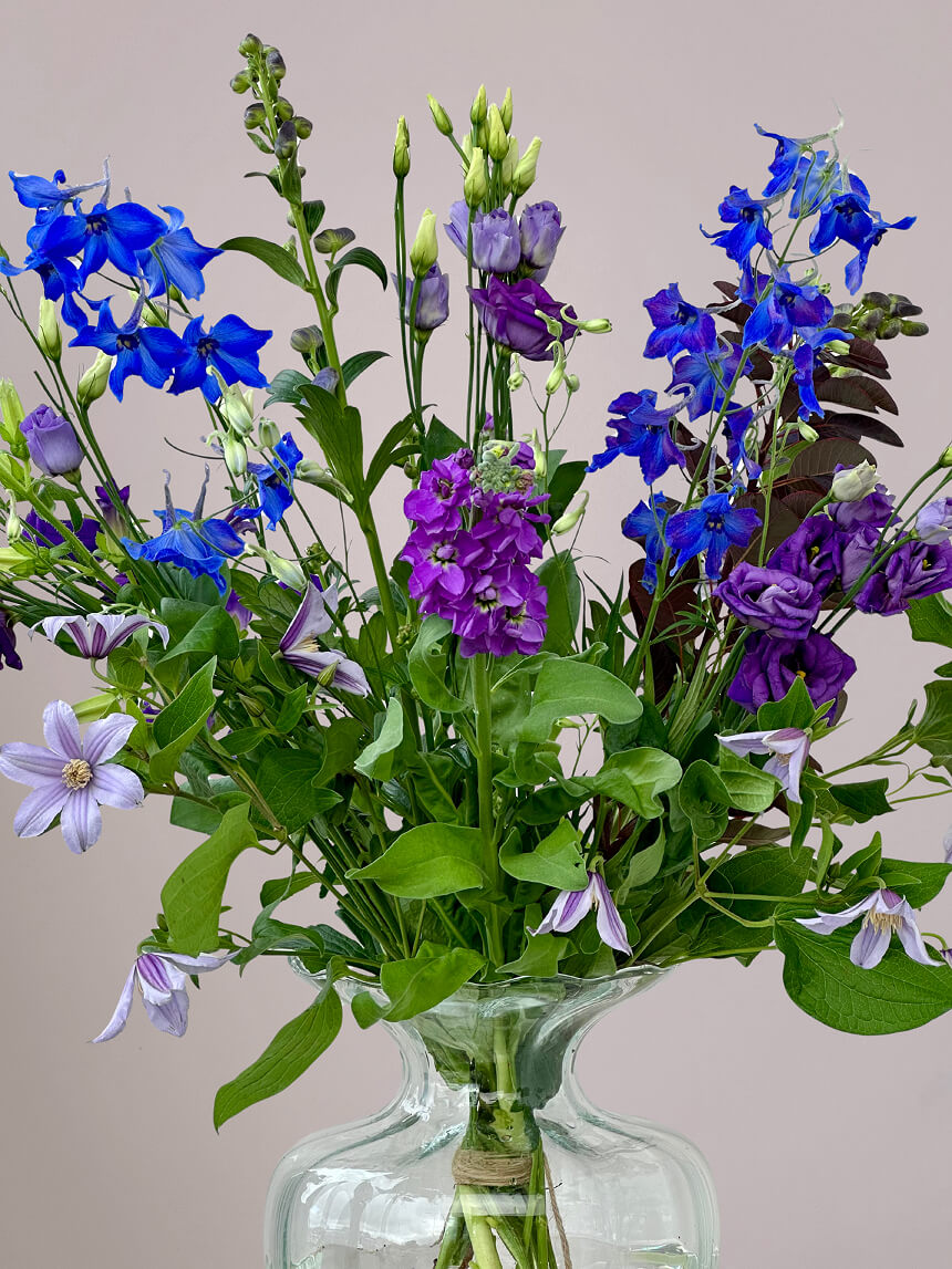 Close-up van Blauw-Paars Veldboeket in kleine vaas met delfinium, eustoma, clematis en monnikskap, fris alledaags boeket in blauwe en paarse tinten