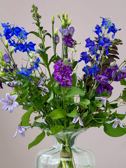 Close-up van Blauw-Paars Veldboeket in kleine vaas met delfinium, eustoma, clematis en monnikskap, fris alledaags boeket in blauwe en paarse tinten