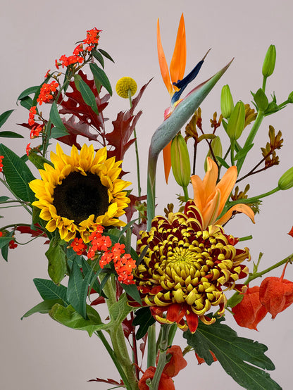 Detail van Luxe Herfstpluk Oranje met zonnebloem, strelizia, craspedia, physalis en lelie, seizoensbloemen in warme oranje- en goudtinten