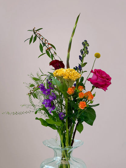 Close-up van Bontepluk boeket in kleine vaas met roze roos, gele celosia, blauwe monnikskap en oranje trosroos, kleurrijk alledaags boeket bezorgen Stadshagen
