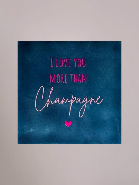 Donkerblauw keramieken tegeltje met felroze tekst “I love you more than champagne” en klein roze hartje