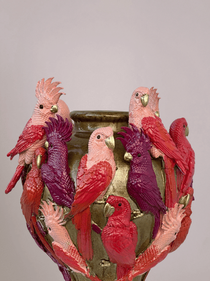 Close-up van kaketoevogel in rood en roze op gouden vaas, met 3D-effect en opvallende details.