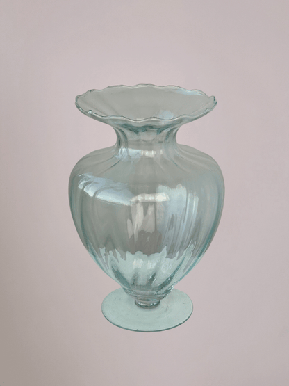 Doorzichtige vaas van boven met diepe ribbels, smalle bovenhals en ronde voet, met lichtroze achtergrond.