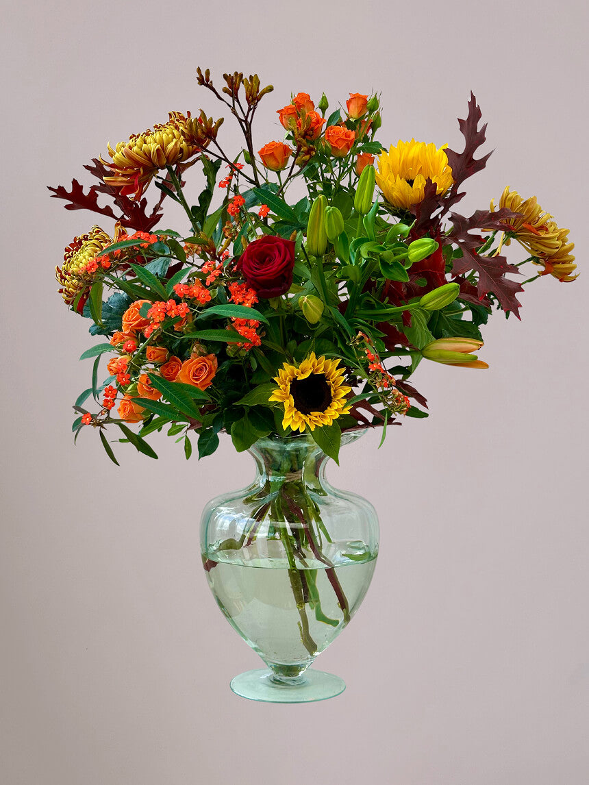 Herfstboeket rond in glazen vaas met zonnebloemen, rode rozen, trosrozen, kangaroepootjes, herfstchrysanten en euphorbia, herfstbloemen in warme kleuren”