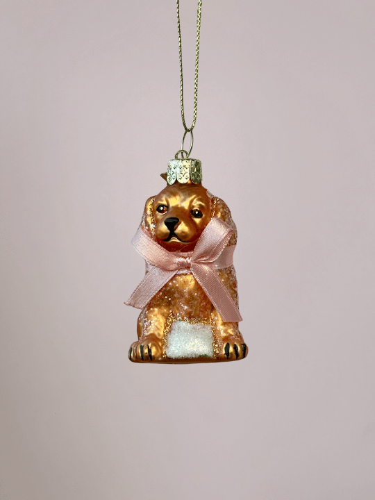 Close-up van Vondels glazen labradoodle kerstbal met mat goudblonde kleur en roze strik op lichtroze achtergrond.