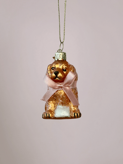 Close-up van Vondels glazen labradoodle kerstbal met mat goudblonde kleur en roze strik op lichtroze achtergrond.