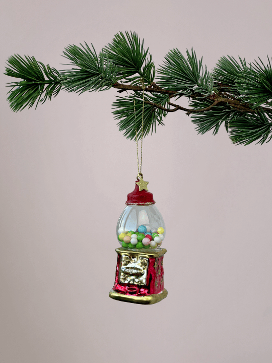 Rode kauwgumbalmachine kerstbal van Vondels met gekleurde kauwgomballen en gouden randen hangend in een kerstboom.