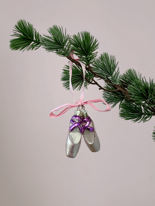 Vondels lichtroze balletschoenen kerstornament met paarse lintjes en glitters hangend in een kerstboom.