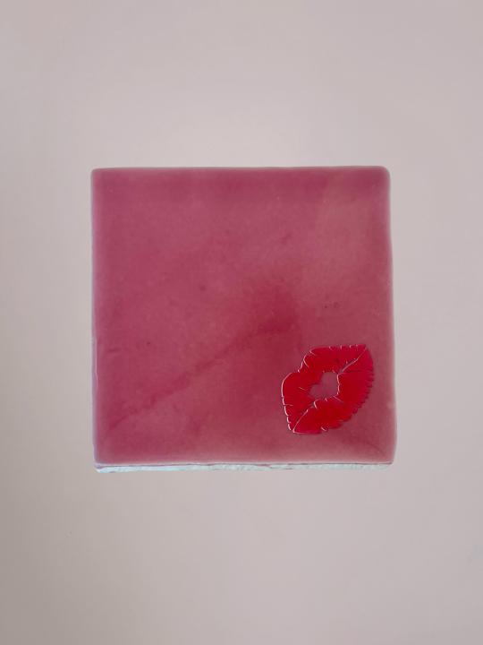 Roze Yett Agenturen tegeltje van 10x10 cm met een rood kusje en glanzende afwerking. Een speels en liefdevol decoratietegeltje.