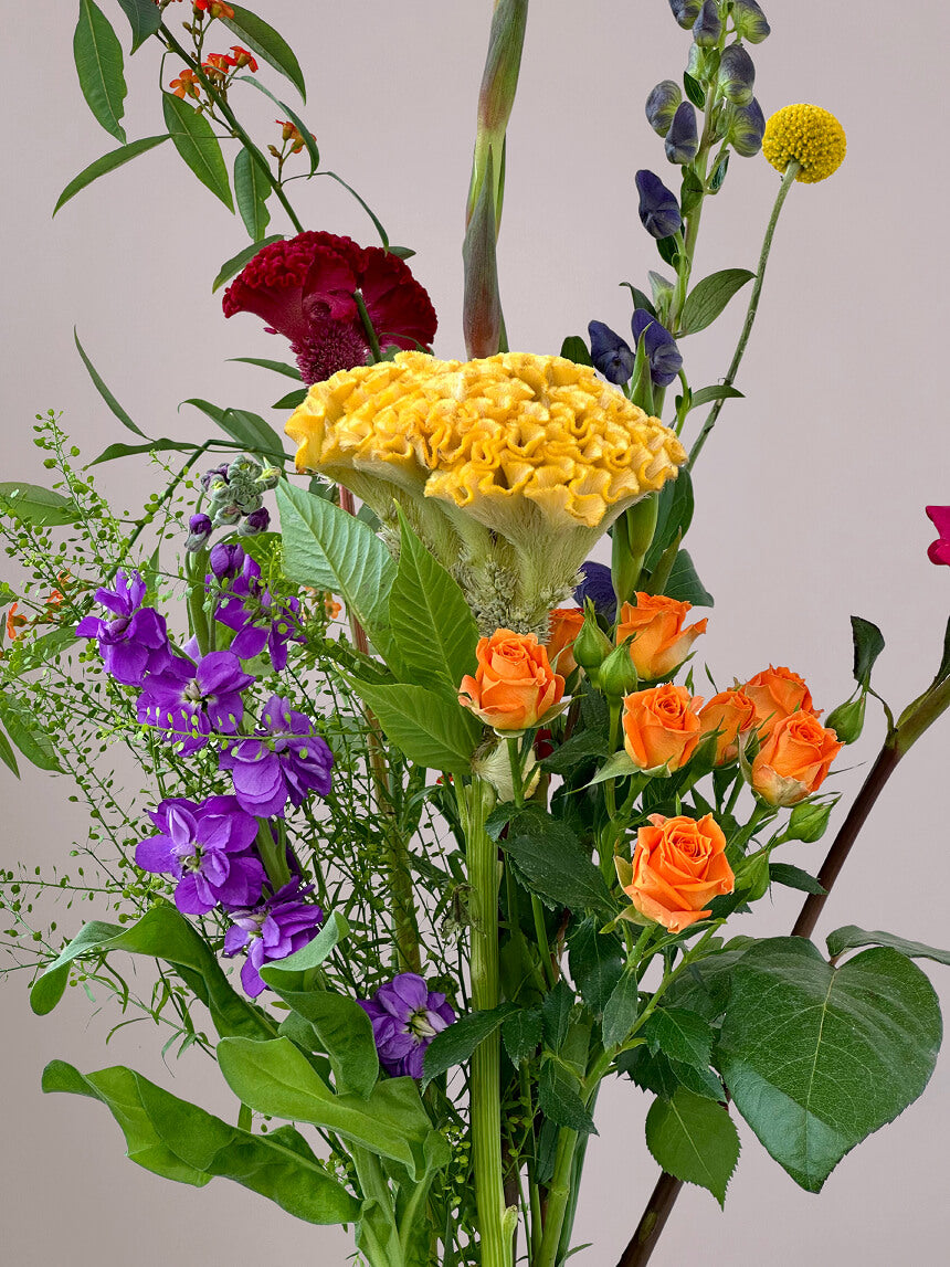 Detail van Bontepluk boeket met roze roos, gele celosia, blauwe monnikskap, oranje trosroos, gladiool en craspedia, fris en kleurrijk