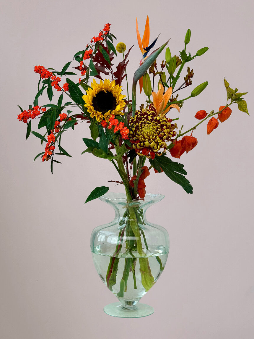 Luxe Herfstpluk Oranje in kleine vaas met zonnebloemen, lelie, strelizia, herfstchrysant, euphorbia, craspedia en physalis