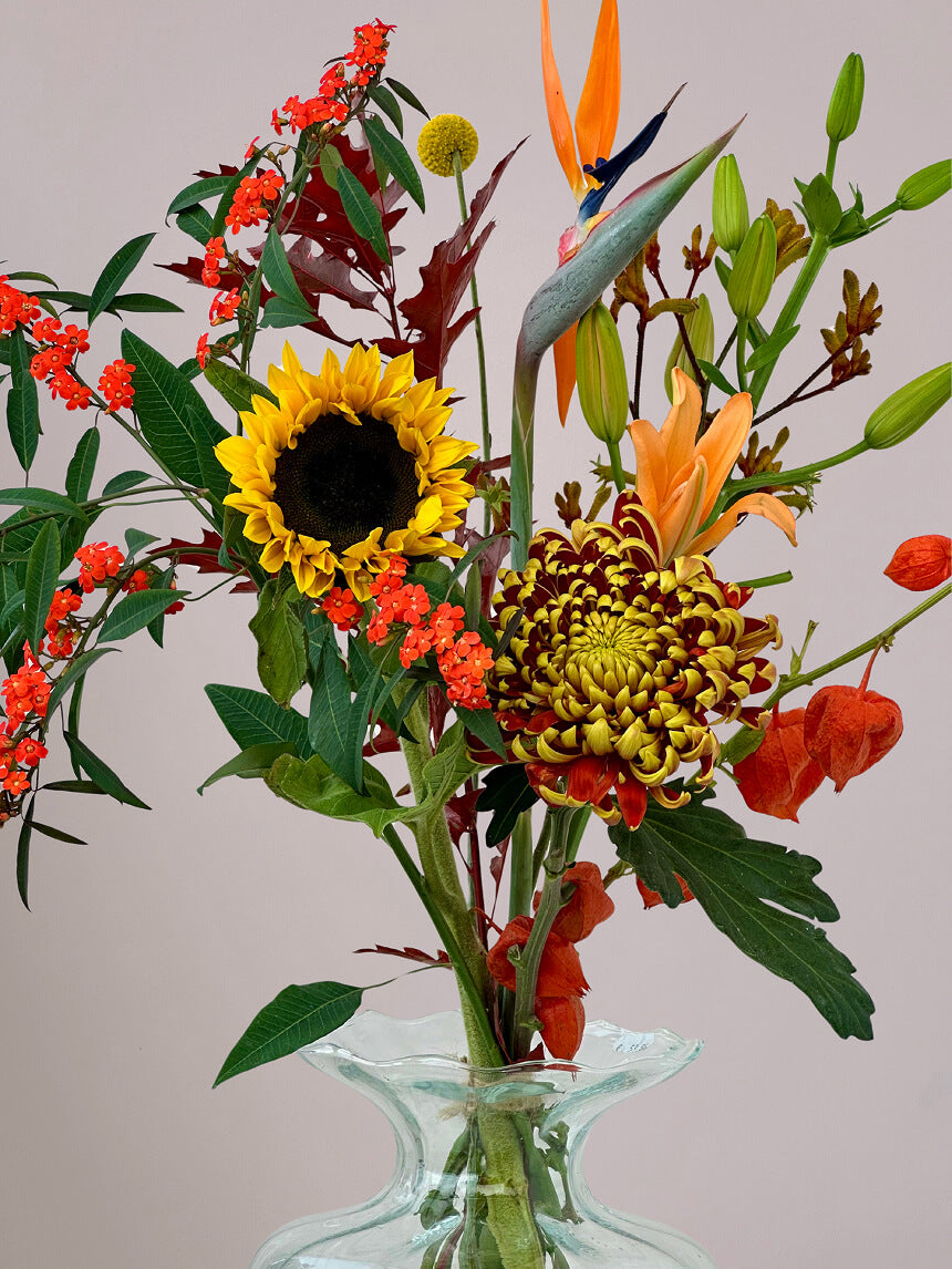 Close-up van herfstboeket Luxe Herfstpluk Oranje in vaas met zonnebloemen, lelie, strelizia, herfstchrysant en physalis, herfstboeket met warme kleuren en textuur