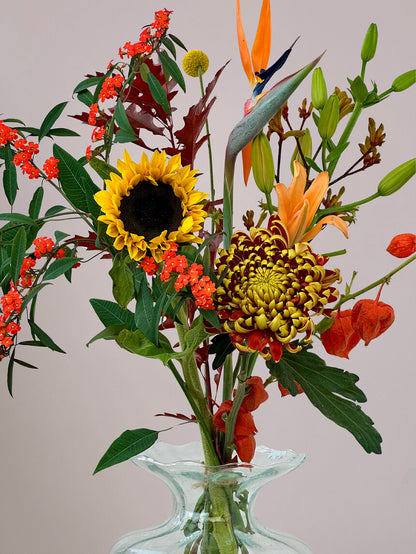 Close-up van herfstboeket Luxe Herfstpluk Oranje in vaas met zonnebloemen, lelie, strelizia, herfstchrysant en physalis, herfstboeket met warme kleuren en textuur