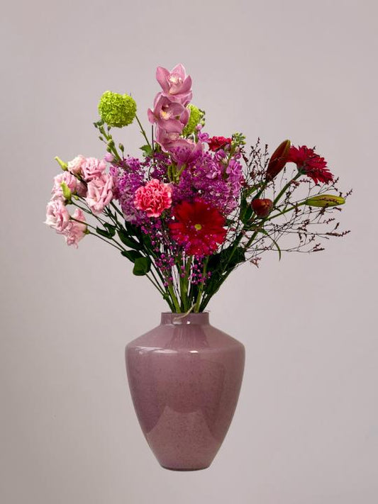 Moederdagboeket met cymbidium, gerbera, anjer, lisianthus, violier, sneeuwbal en lelie in roze tinten in een roze vaas.