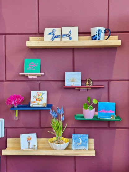 Kleurrijke wandplankjes van Studio Mippe aan de muur, gestyled met tegeltjes, bloemen en accessoires in verschillende kleuren.