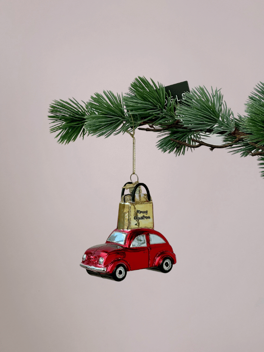 Vondels rode auto kerstornament met goud cadeautasje en glitters hangend in een kerstboom.
