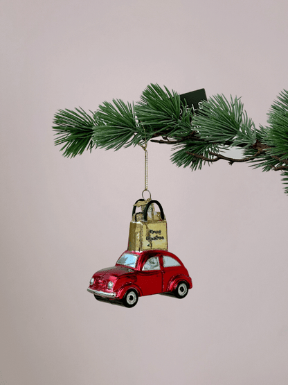 Vondels rode auto kerstornament met goud cadeautasje en glitters hangend in een kerstboom.