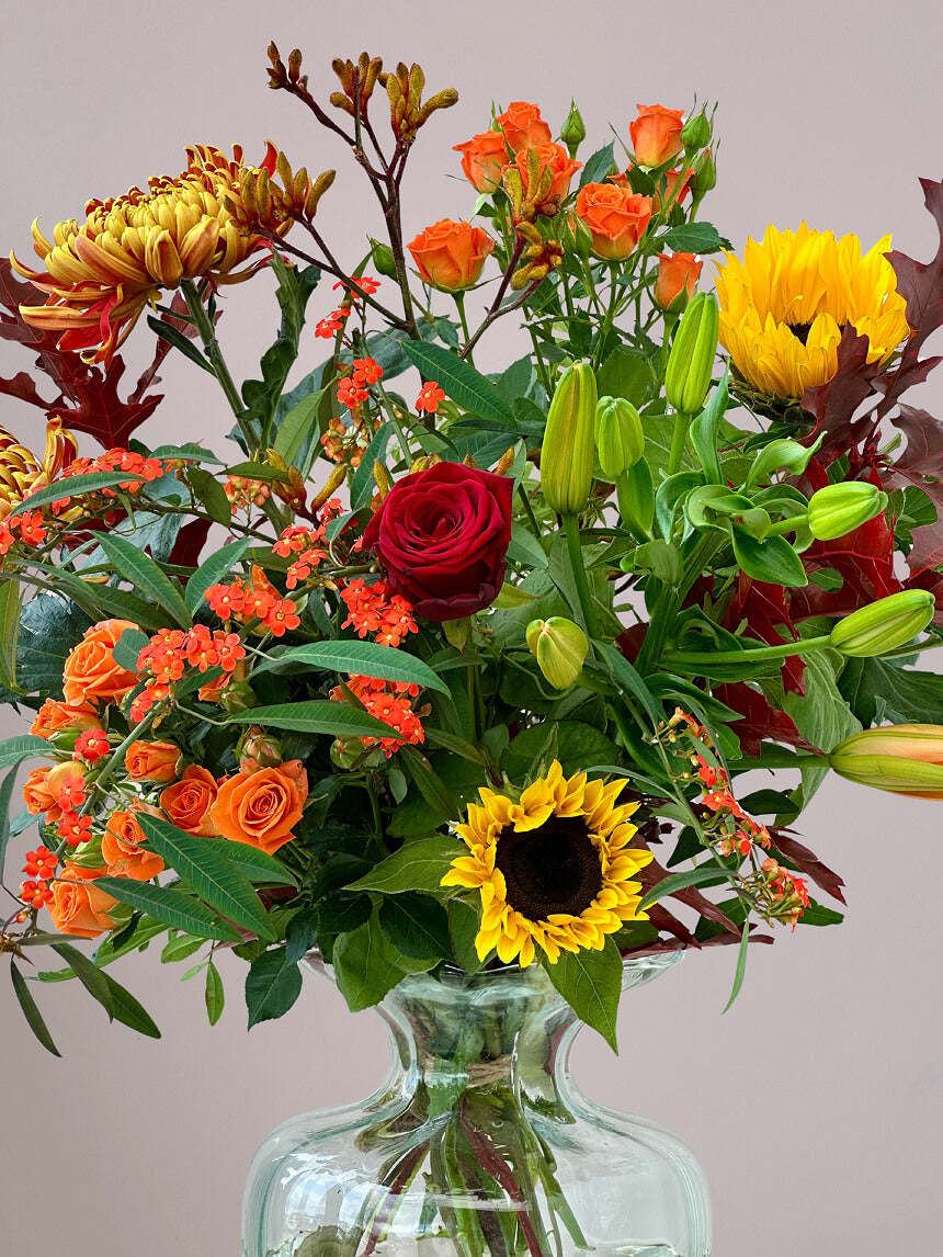 Close-up van herfstboeket rond in ronde vaas met zonnebloemen, rode rozen, trosrozen, kangaroepootjes en herfstchrysanten, perfect voor herfstdecoratie