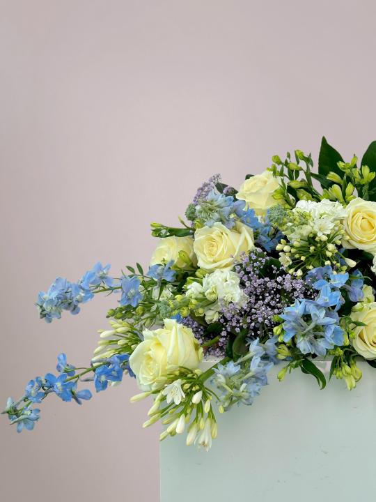 Liggend rouwboeket voor op kist met blauwe en witte bloemen en groene bladeren in Zwolle. 