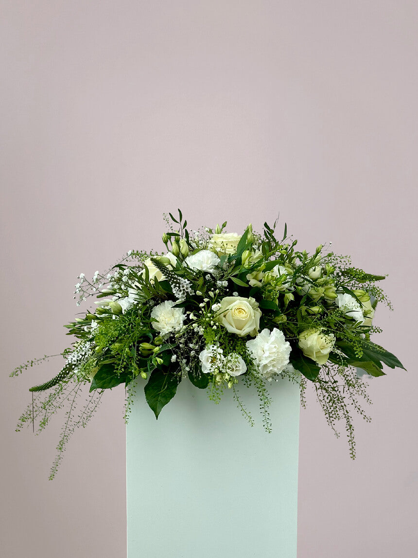 Rouwboeket wit met zachte bloemen in ronde compositie, op tafel geplaatst