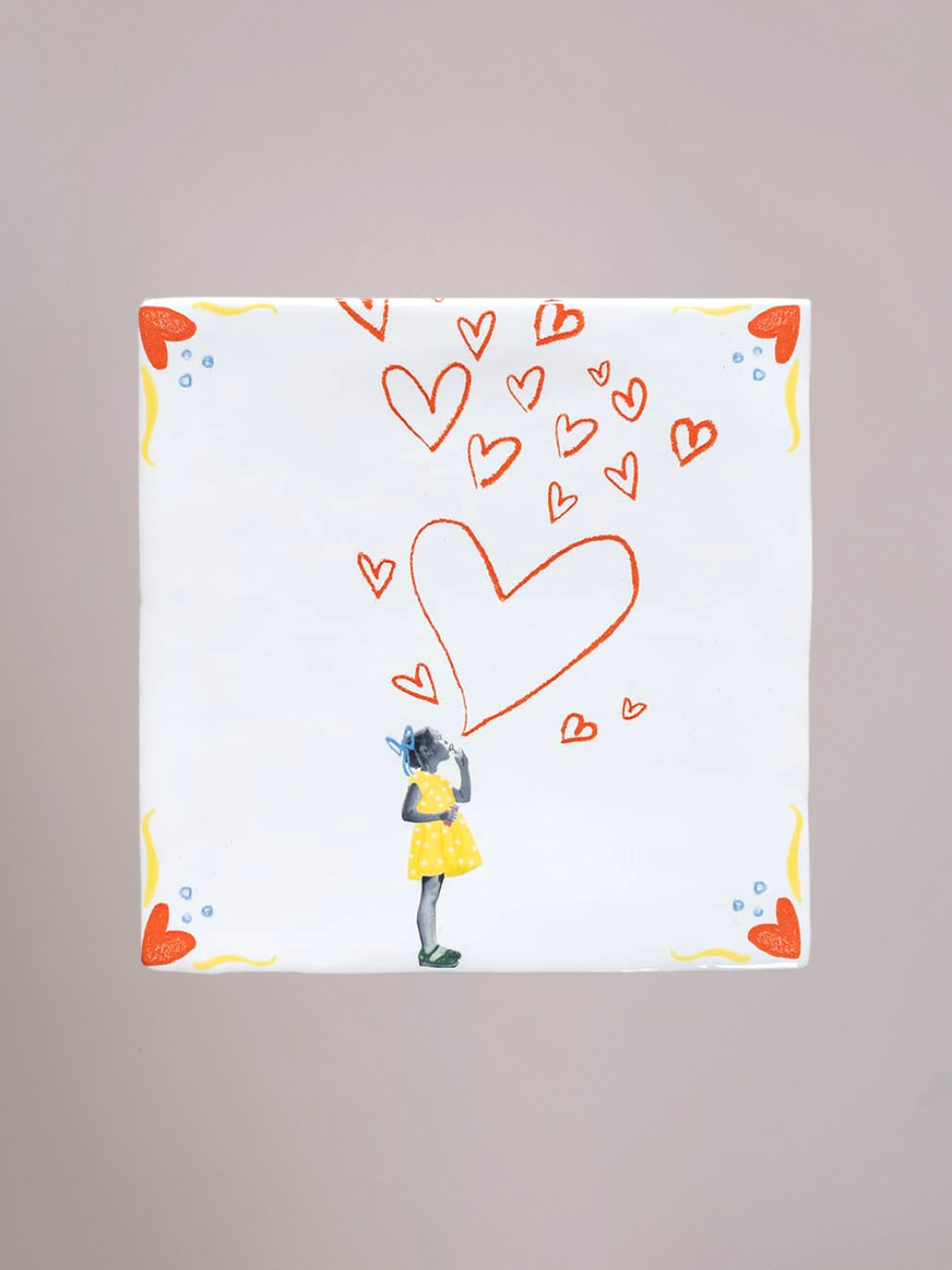 Tegel Spread the Love met een meisje in een gele jurk dat hartjes de lucht in blaast, symbool voor liefde, geluk en het delen van vreugde.