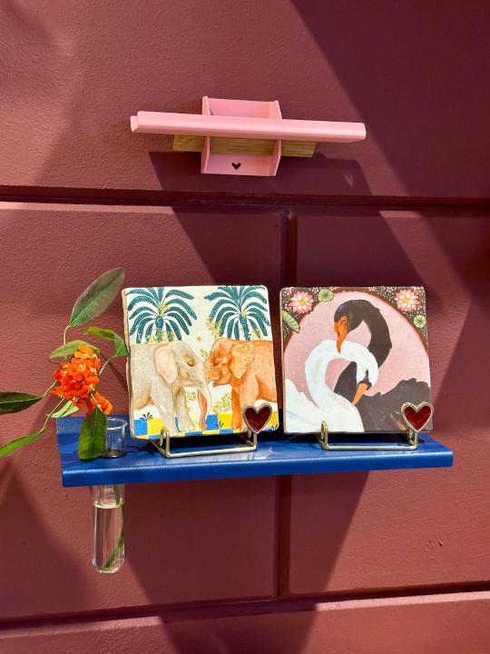 StoryTiles tegeltjes met dierenillustraties in gouden houders op blauwe wandplank, gestyled met oranje bloem bij Anja Bloementrends