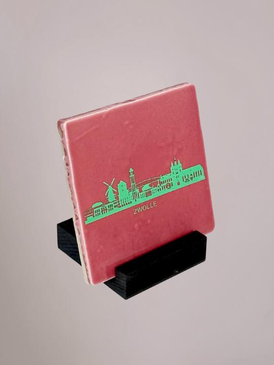 Kleurrijk tegeltje dat stijlvol wordt weergegeven in een zwarte houten tegelhouder van Yett Agenturen.