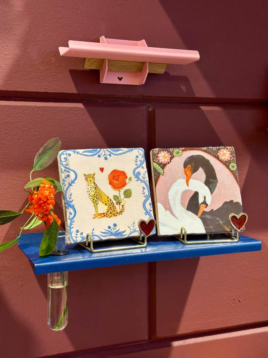 Tegeltjes met panter en zwanen in gouden tegelhouders op blauwe wandplank met reageerbuisje bij Anja Bloementrends