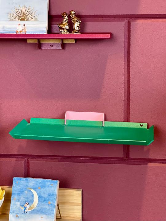 Groene tray aan de muur met roze bracket, minimalistisch gestyled met een kleurrijk tegeltje.