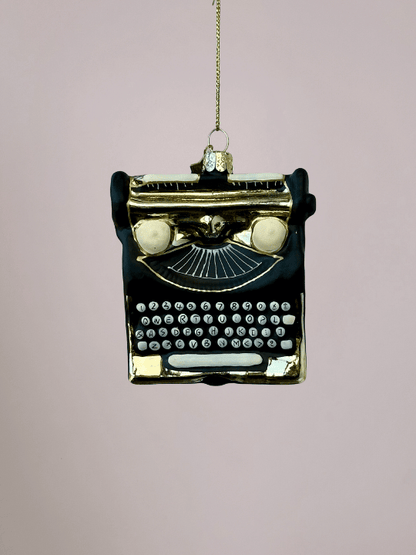 Close-up van Vondels zwarte typemachine kerstornament met gouden details op roze achtergrond.