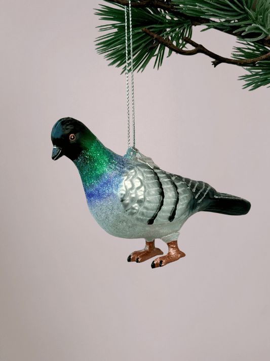 Close-up van Vondels kerstbal stadsduif met grijs, wit, zwart, groen en blauw in de nek en oranje poten op lichtroze achtergrond.