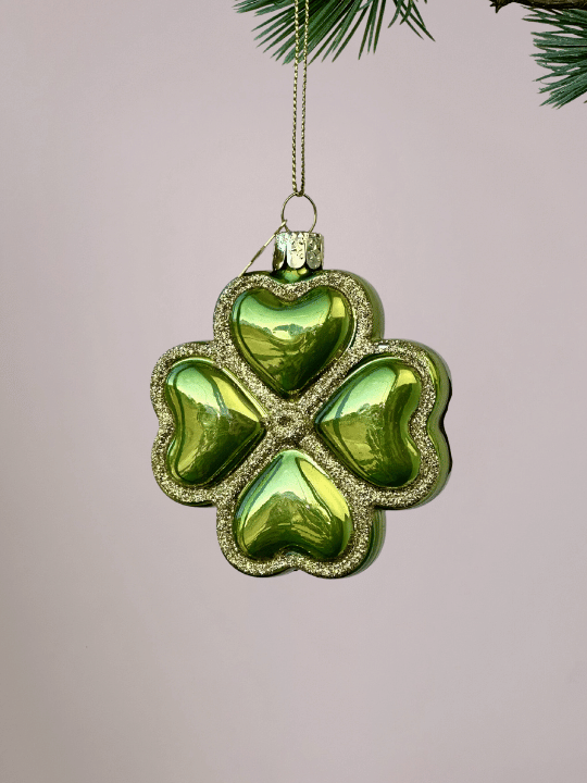 Close-up van Vondels groen geluksornament klavertje vier met gouden glitterranden op lichtroze achtergrond.