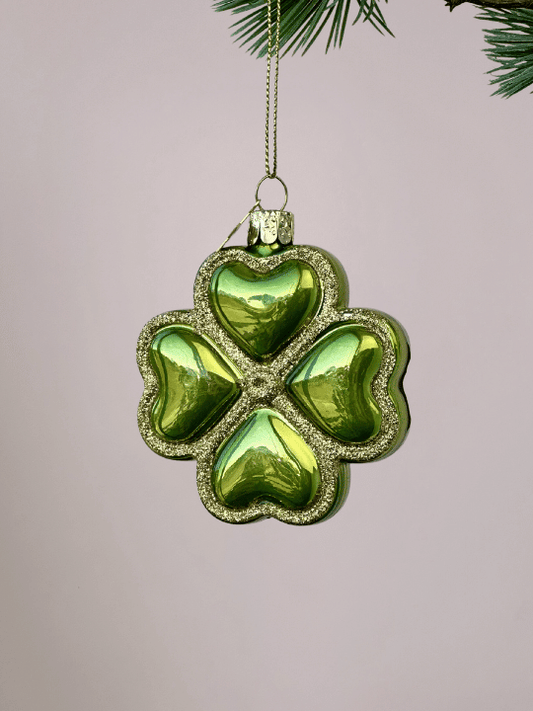 Close-up van Vondels groen geluksornament klavertje vier met gouden glitterranden op lichtroze achtergrond.