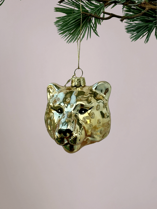 Close-up van Vondels panterhoofd goud glazen kerstbal met zwarte details voor ogen, neus en mond, bijzondere en gekke kerstbal voor lichtroze achtergrond