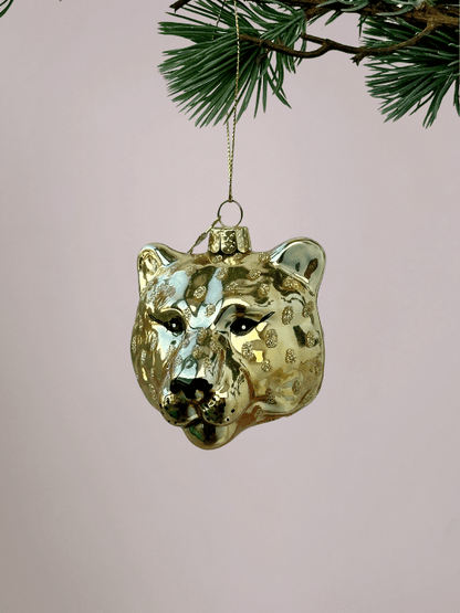 Close-up van Vondels panterhoofd goud glazen kerstbal met zwarte details voor ogen, neus en mond, bijzondere en gekke kerstbal voor lichtroze achtergrond