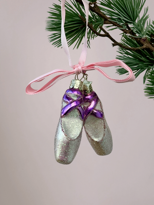 Close-up van lichtroze balletschoenen kerstornament Vondels met paarse en roze lintjes en glitters op lichtroze achtergrond.