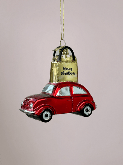 Close-up van Vondels  rode auto kerstornament met goud cadeautasje en glitters op een roze achtergrond.