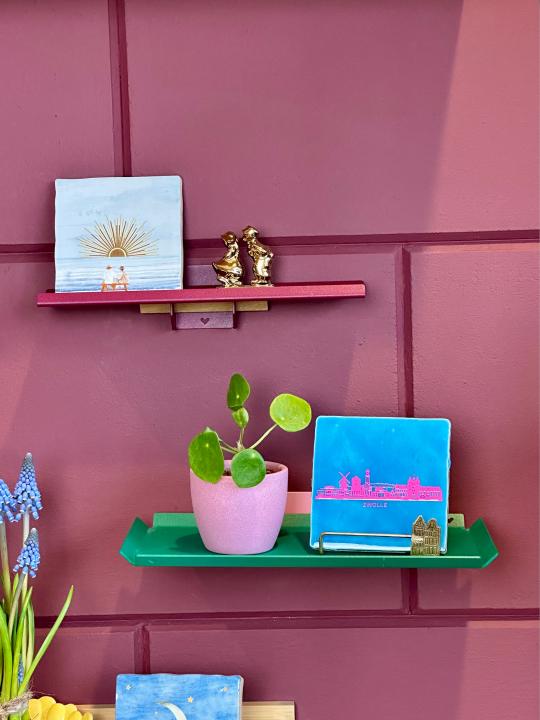 Groene tray en roze wandplankje aan de muur, gestyled met een plant en kleurrijk tegeltje.