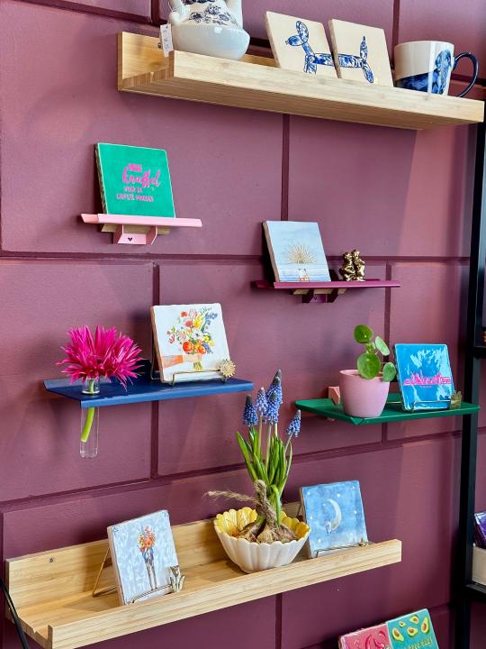 Zijaanzicht van kleurrijke wandplankjes van Studio Mippe met tegeltjes, bloemen en woonaccessoires in een creatieve opstelling.