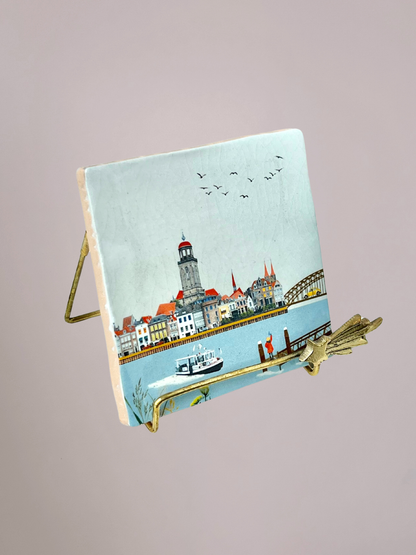 StoryTiles tegeltje Zwaaiend Naar Deventer met meisje aan rivier dat naar stad zwaait en stadsgezicht op keramisch tegeltje
