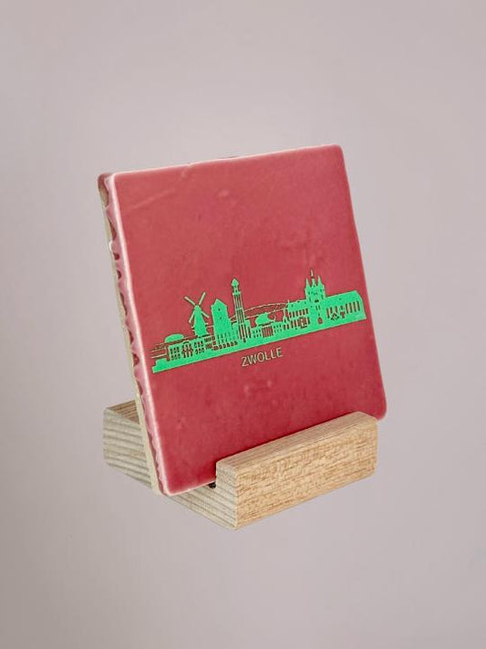 Roze mintkleurig Zwolle-tegeltje dat trots in een houten houder staat te stralen, klaar om je interieur nét wat vrolijker te maken.